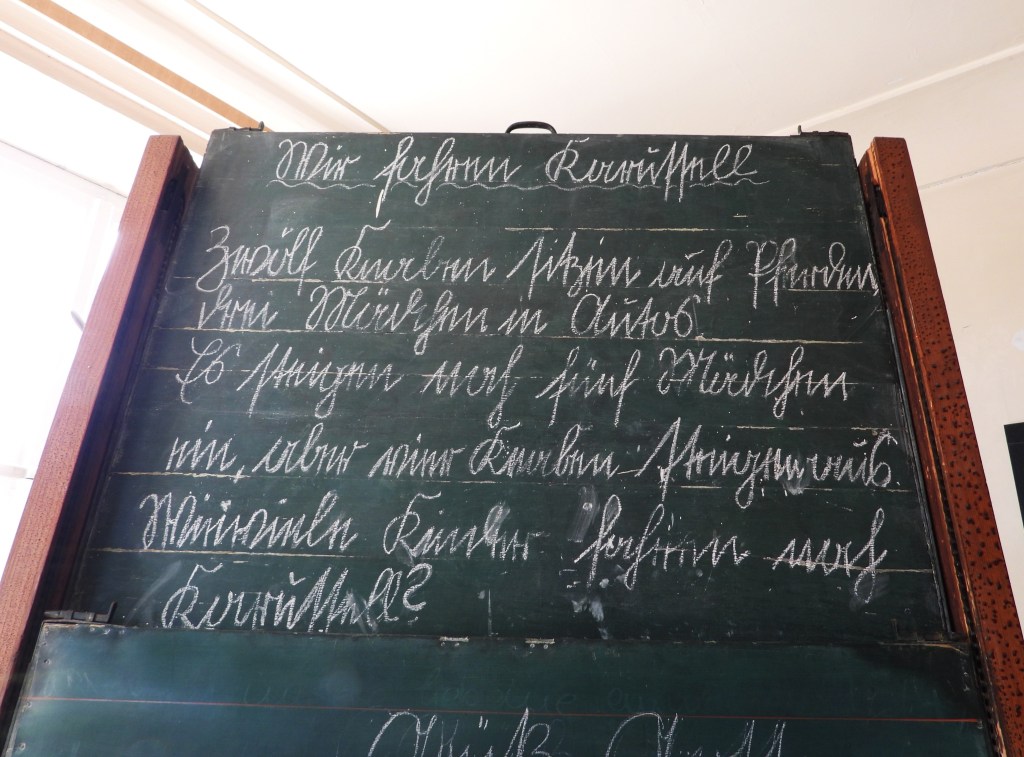 Eine Schultafel mit handgeschriebener Sütterlinschrift, die eine Rechenaufgabe zeigt.