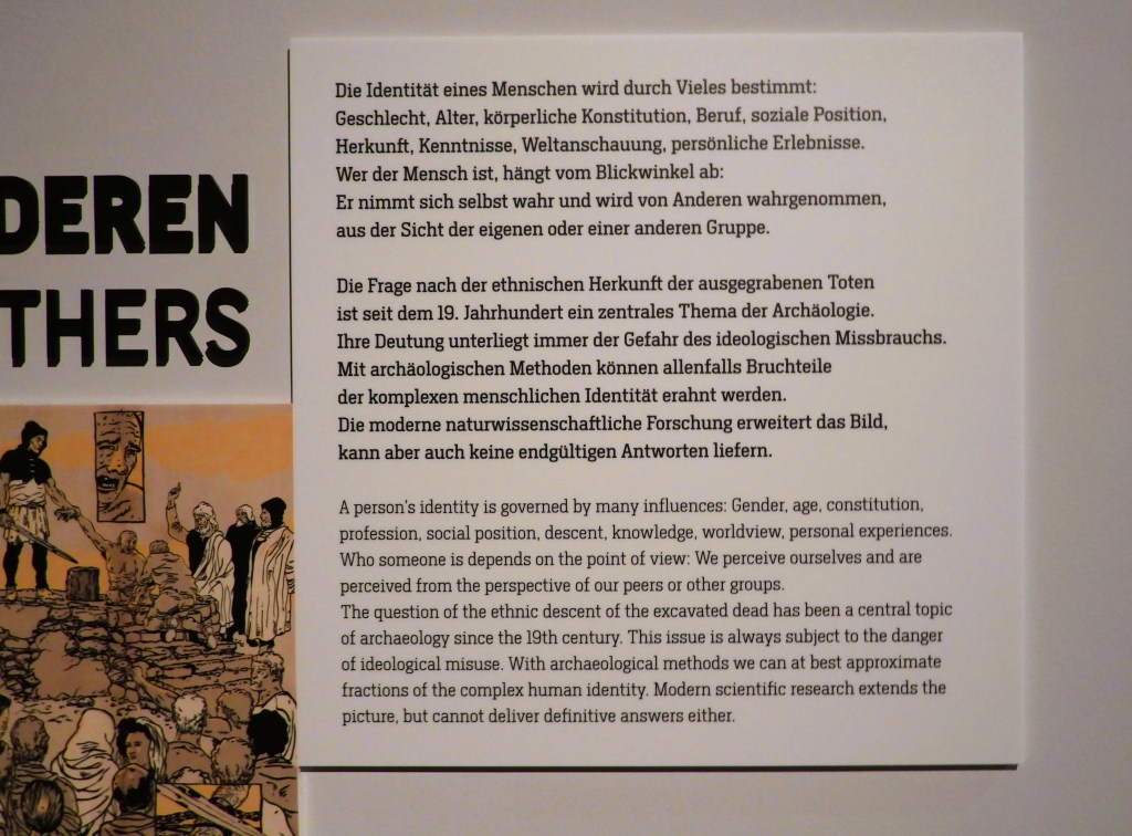 Tafel mit Informationen zur Identität von Menschen, umgeben von Illustrationen und grafischen Elementen, die Aspekte der Archäologie und ethnischen Herkunft darstellen.