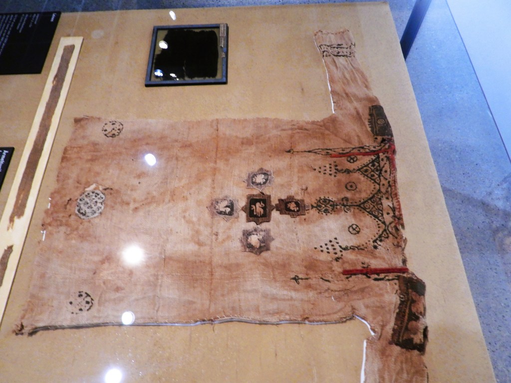 Eine ägyptische Kindertunika aus Wolle und Leinen, die unter Panzerglas ausgestellt ist, zeigt kunstvolle Verzierungen und ist über 1600 Jahre alt.