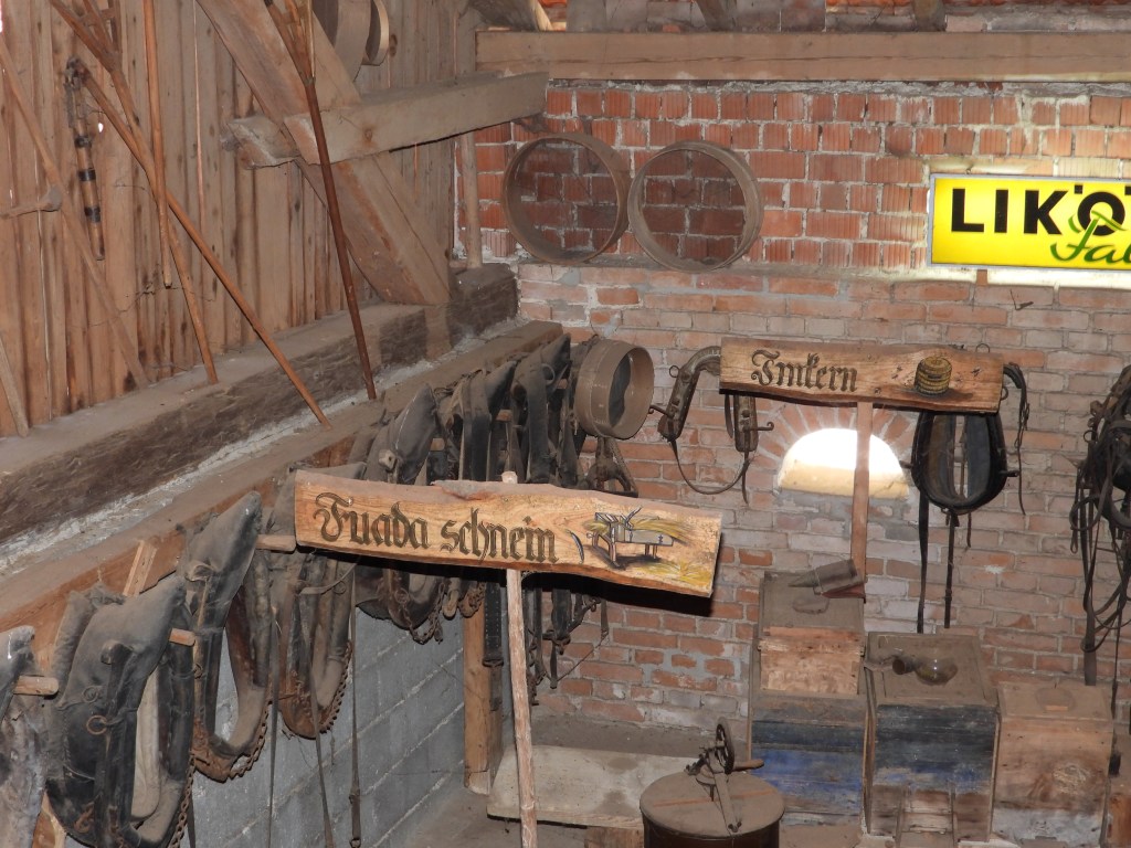 Ein Blick ins Bauernhofmuseum mit historischen Geräten und Utensilien, darunter verschiedene Geschirre an der Wand und Holzregale.