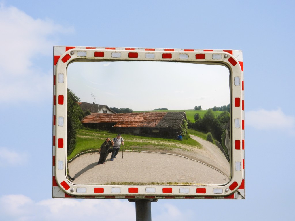 Spiegel mit reflektierenden Bildern einer ländlichen Szenerie, einschließlich einer Scheune und zwei Personen, die auf einem Weg stehen.