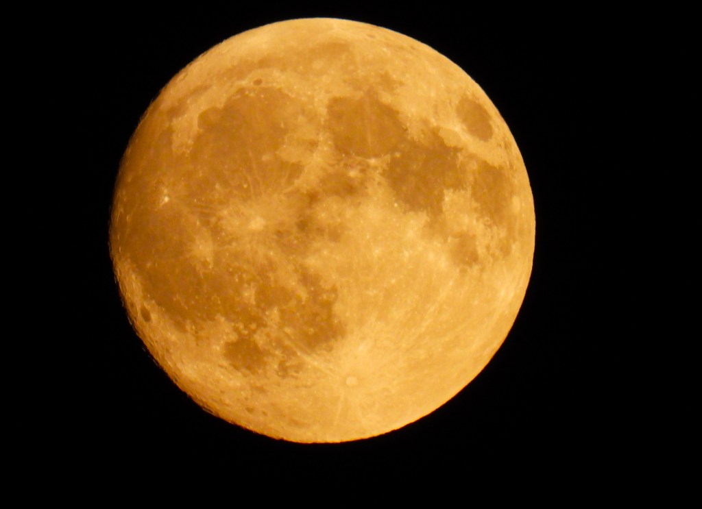 Detailaufnahme des Mondes mit sichtbaren Kratern auf der Oberfläche, hervorgehoben durch eine orangefarbene Erscheinung vor einem schwarzen Hintergrund.