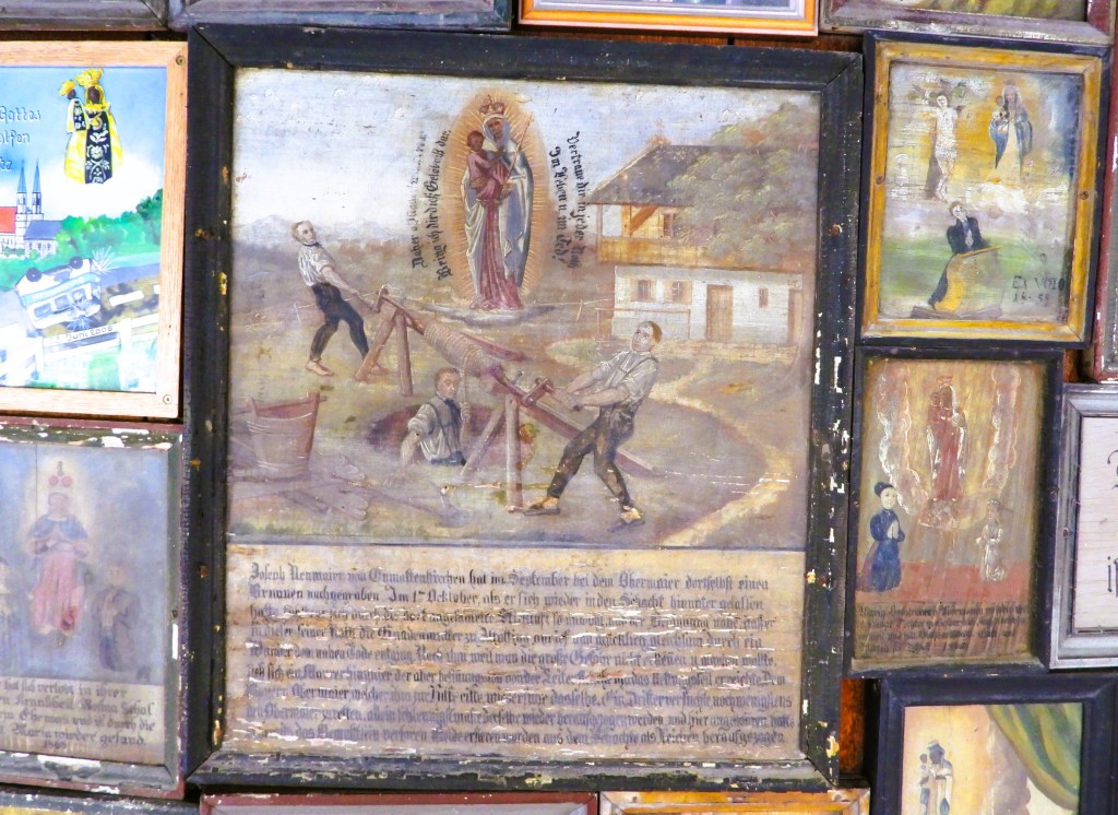 An ornate display of votive paintings on a wall, depicting various scenes of gratitude and protection in the context of faith. The central piece shows individuals engaged in a rescue effort, surrounded by other smaller images reflecting personal stories and historical events.