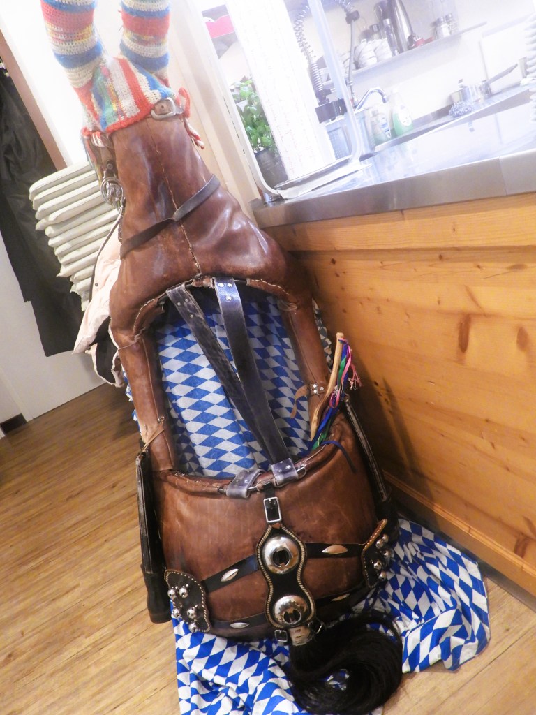 Ein traditioneller Reitsattel für den "Bräunlreiter", verziert mit bunten Accessoires, auf einem Tisch neben einer bayerischen Tischdecke.