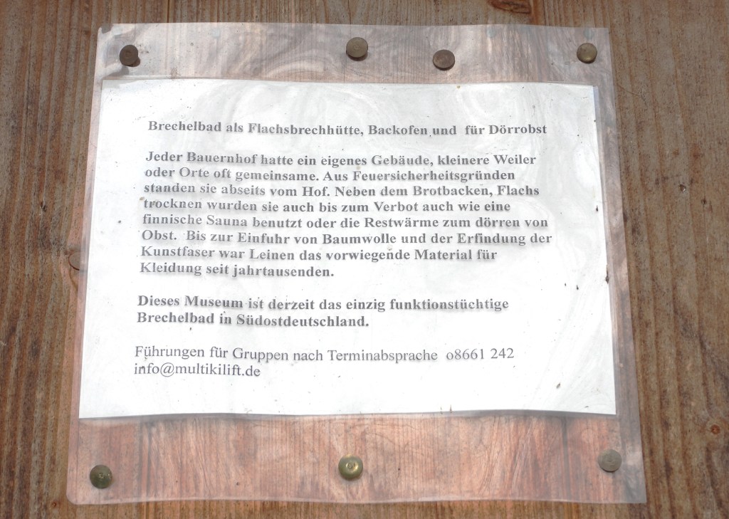 Tafel mit Informationen über das Brechelbad Museum in Stöttham, das die traditionelle Flachsverarbeitung und die Verwendung des Gebäudes erklärt.