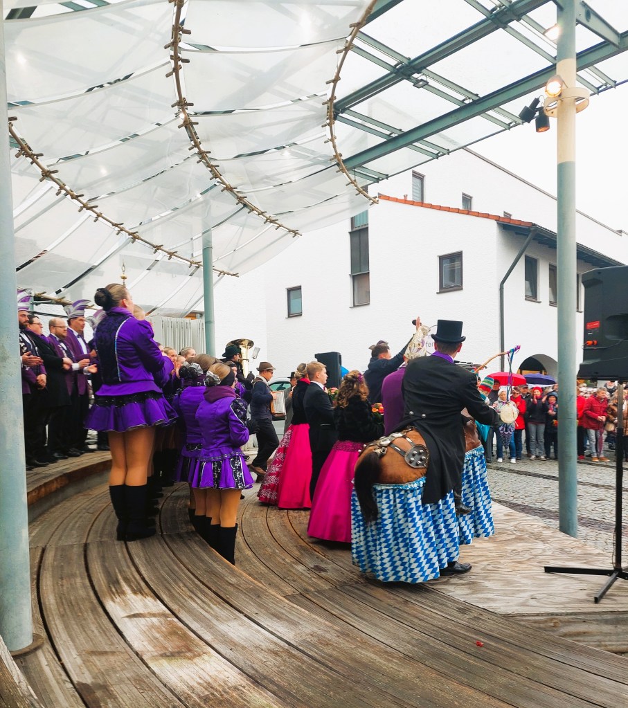 Menschen in bunten Kostümen und Hüten versammeln sich auf einer Bühne während des Faschingauftakts, um eine Aufführung zu genießen.