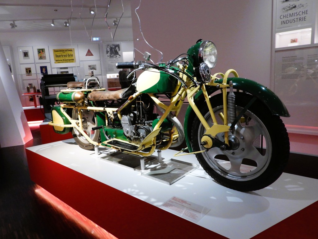 Ein historisches Motorrad aus dem Motorenwerk Albin Liebisch, ausgestellt im Sudetendeutschen Museum, umgeben von weiteren Exponaten.