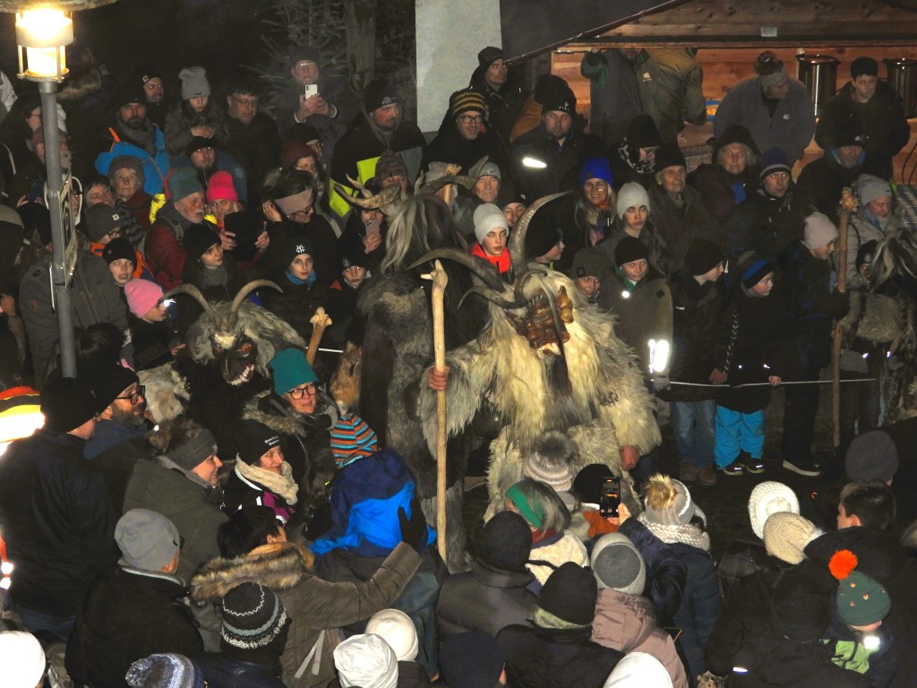 Eine Menschenmenge schaut dem Perchtenlauf in Bad Birnbach zu, während maskierte Teilnehmer mit kunstvollen Masken und Tierkostümen Szenen aufführen.
