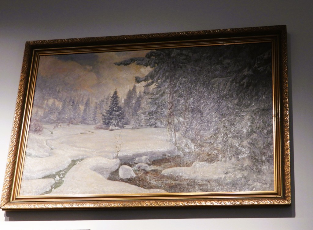 Ein Landschaftsgemälde mit schneebedeckten Bäumen und sanften Hügeln, eingekapselt in einem goldfarbenen Rahmen.