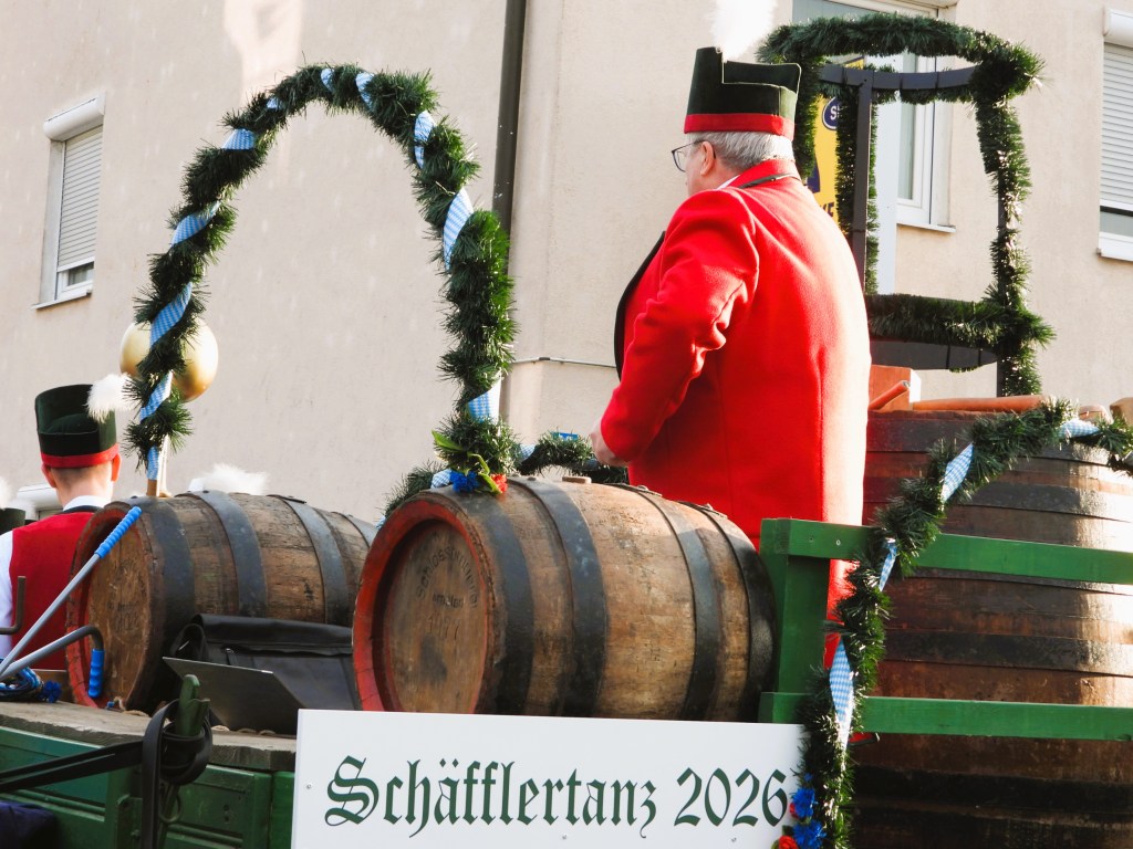 Ein Mann in rotem Outfit auf einem Wagen, umgeben von Holzfässern und festlicher Dekoration während einer Veranstaltung.