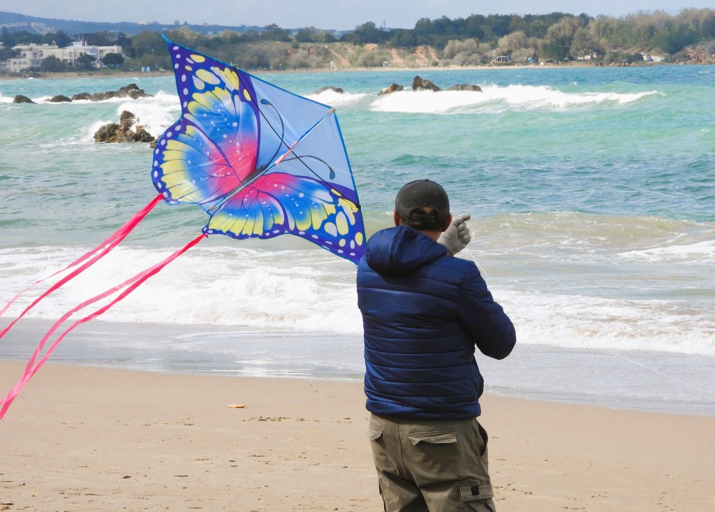 Ein Mann fliegt einen bunten Schmetterlingsdrachen am Strand, während die Wellen im Hintergrund schwappen.