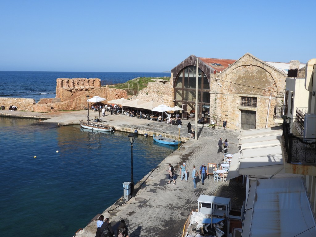 Einmalige Hafenansicht mit historischen Mauern, Cafés mit Sonnenschirmen und Menschen, die am Ufer entlang spazieren.