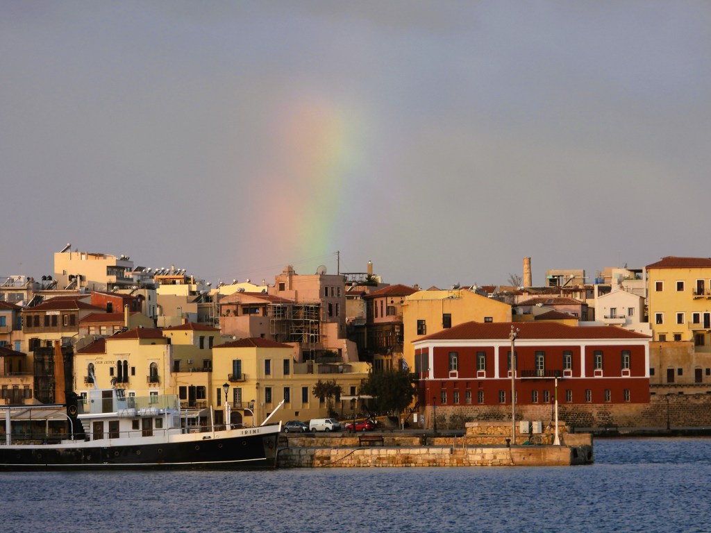 Blick auf eine malerische Küstenstadt mit bunten Häusern und einem Regenbogen am Himmel.