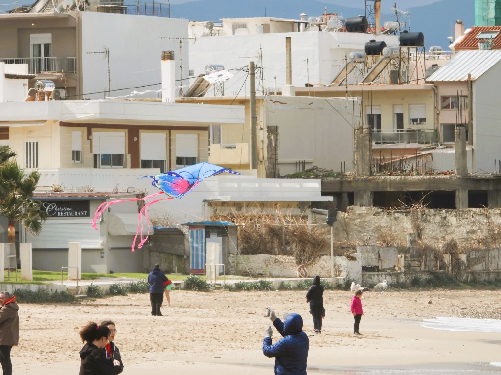 Ein bunter Drachen fliegt über einem Strand, während Menschen in warmer Kleidung am Ufer stehen.