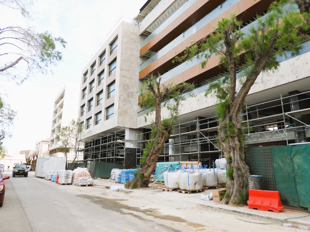 Bauarbeiter in der Nähe eines modernen Gebäudes, das sich im Bau befindet, mit Gerüst und Baumkonstruktionen am Straßenrand.