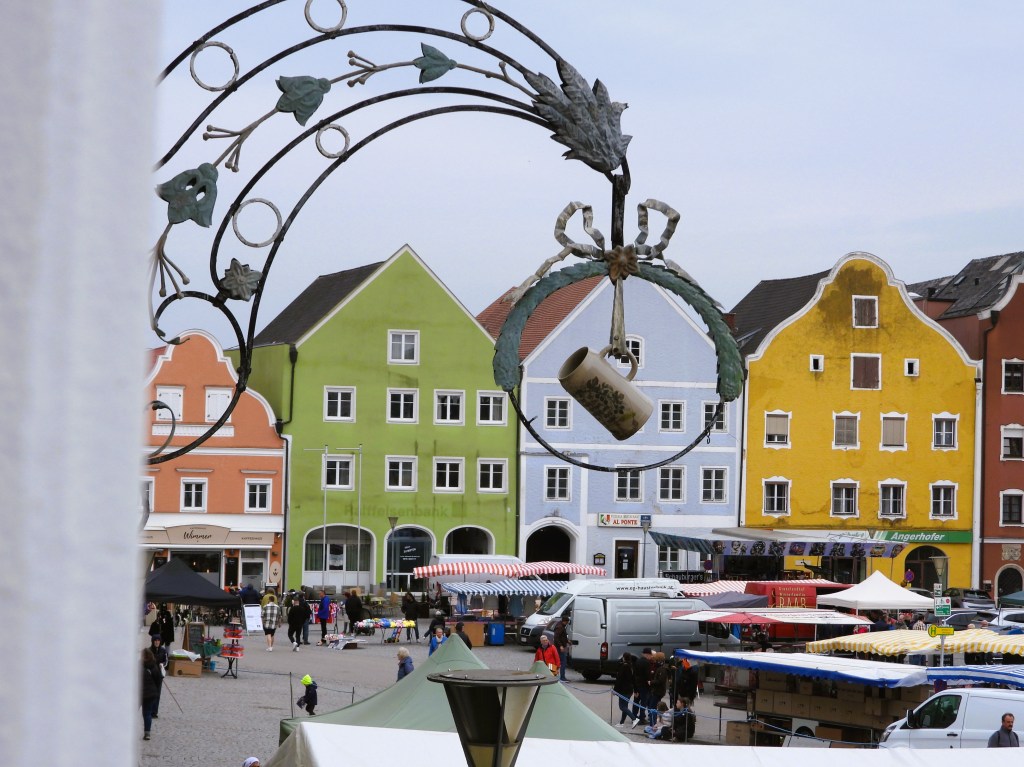 Eine Aussicht auf einen Marktplatz mit bunten Gebäuden, einem kunstvollen Wandschmuck und Marktständen.