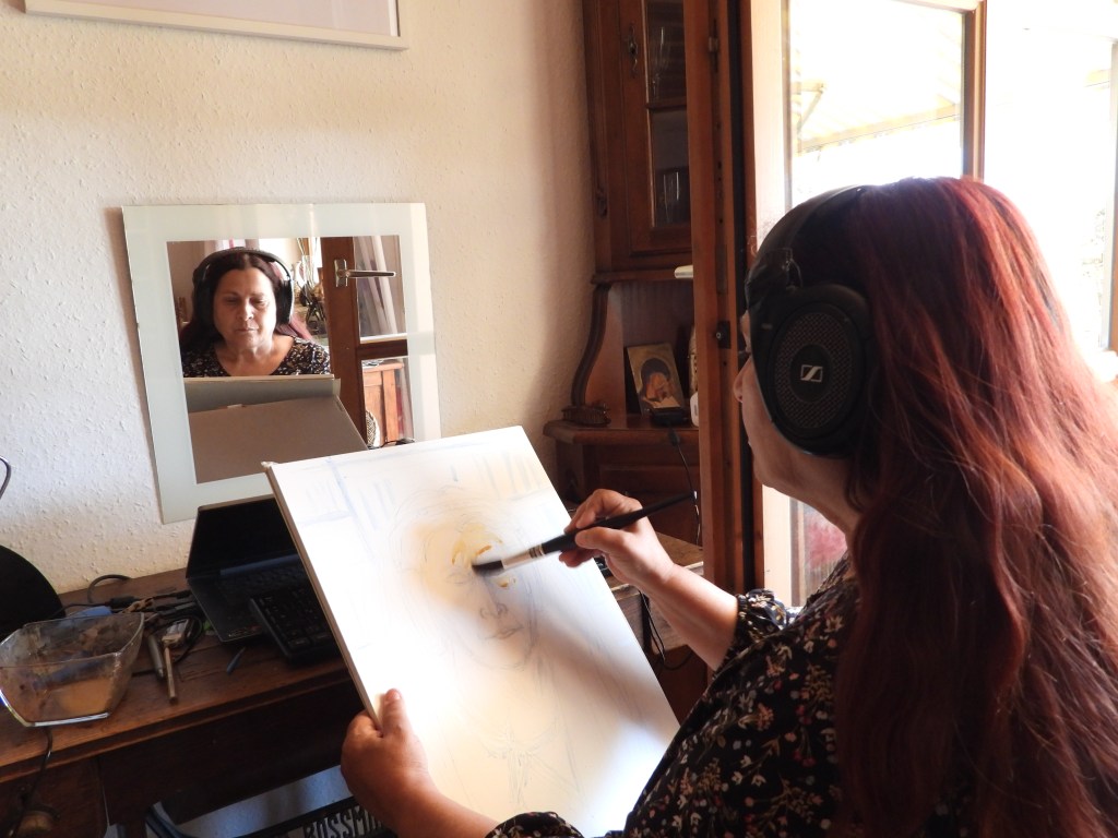 Eine Frau malt ein Selbstporträt, während sie Kopfhörer trägt, und betrachtet ihr Spiegelbild auf einem Tisch. Im Hintergrund sind Möbel und andere Gegenstände zu sehen.