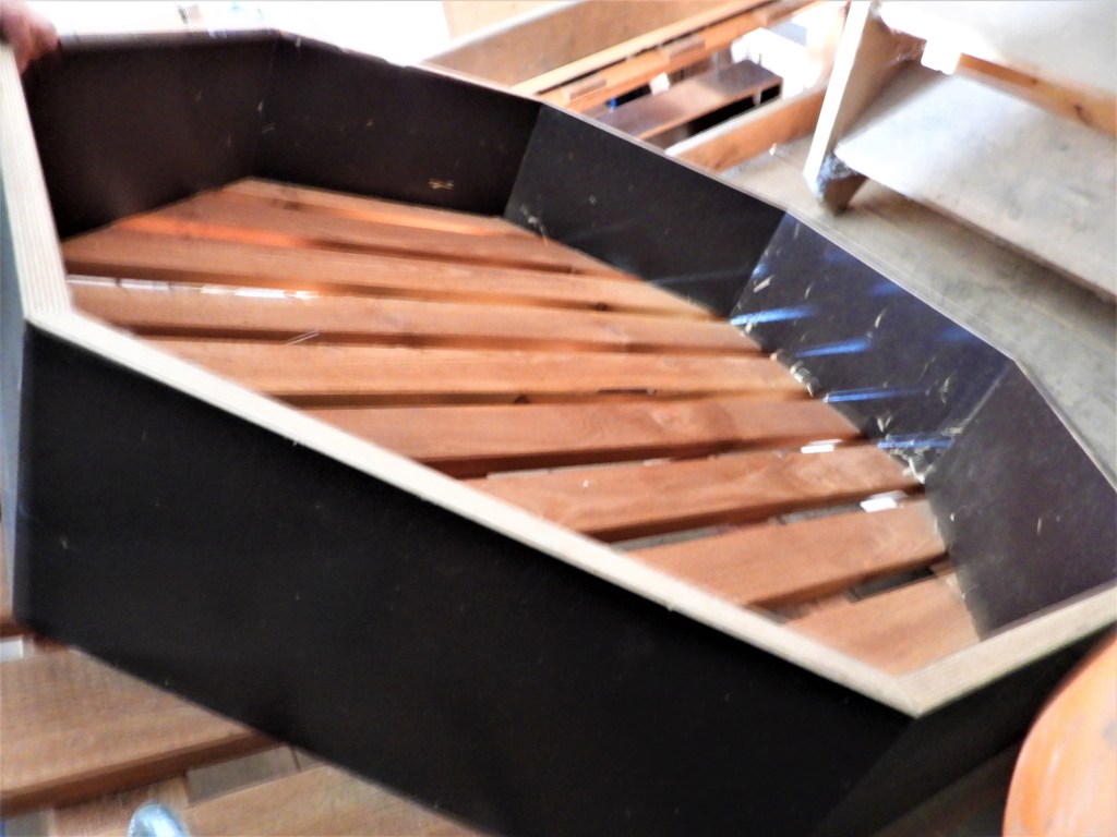 Ein Holzboot mit einer schwarzen Außenwand und Holzlatten im Inneren, das in einer Werkstatt gehalten wird.