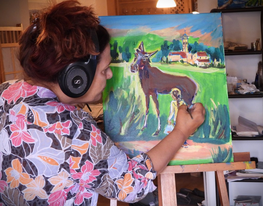 Eine Frau mit Kopfhörern malt ein farbenfrohes Bild mit einem Pferd und einem Kind in einer Landschaft.