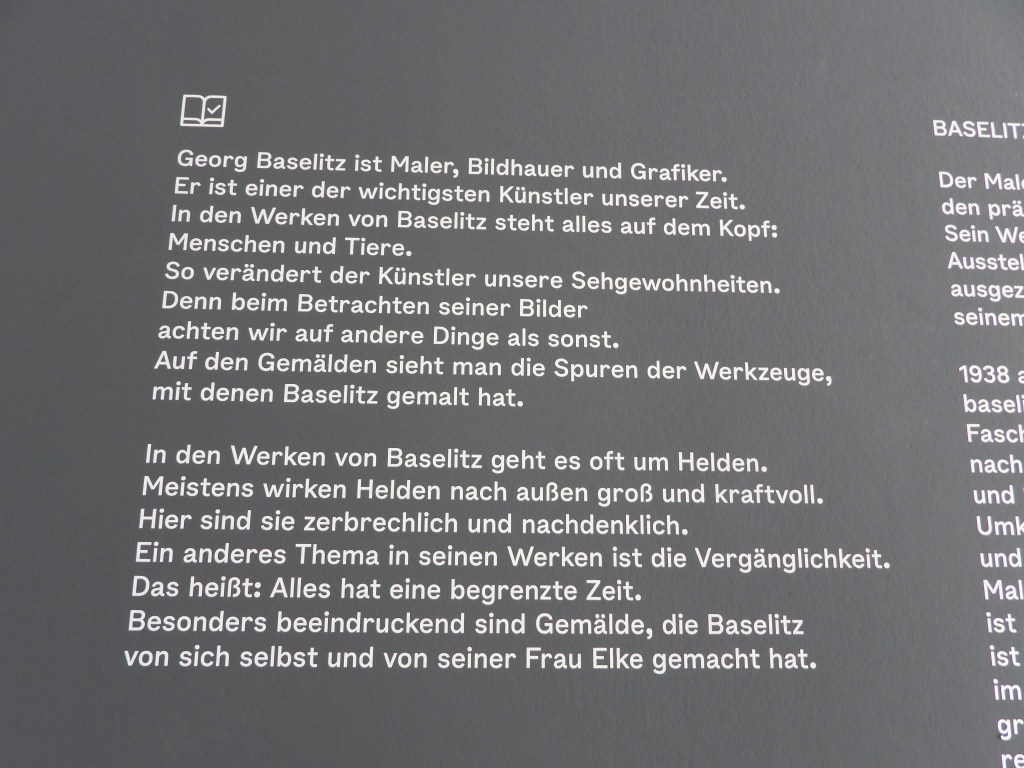Textuelle Beschreibung über den Künstler Georg Baselitz, seine Werke und Themen, die auf einem Ausstellungstext präsentiert werden.