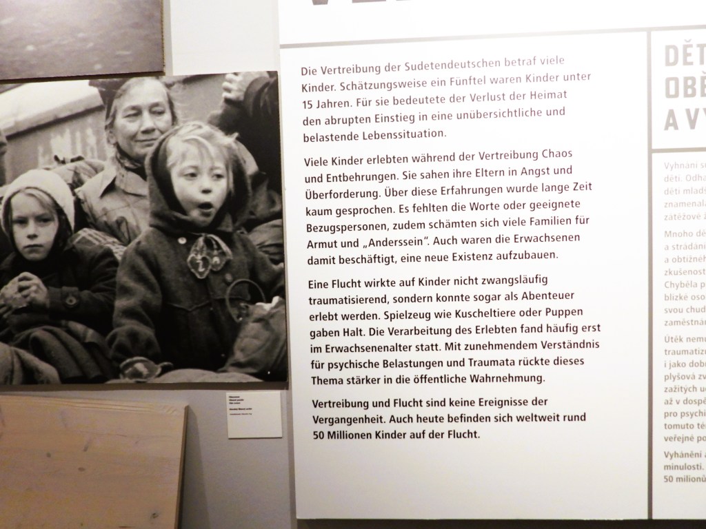 Eine Informationstafel, die über die Vertreibung der Sudetendeutschen und die Auswirkungen auf Kinder informiert. Sie zeigt Kinder mit besorgten Gesichtsausdrücken, die in einer belastenden Lebenssituation sind.