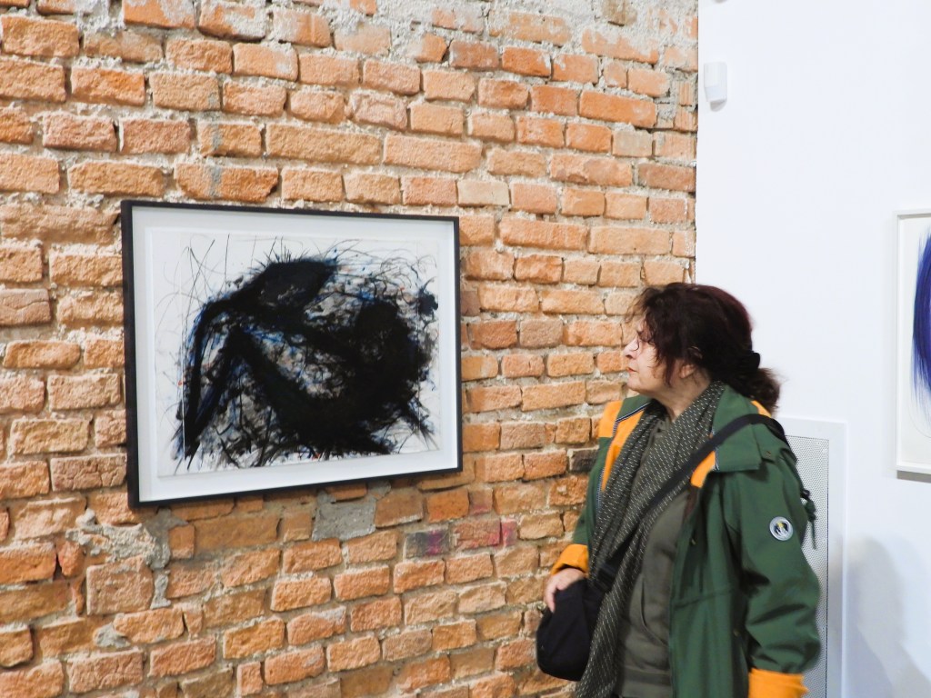 Eine Person steht vor einem schwarzen abstrakten Gemälde in einem Raum mit einer roten Ziegelwand.